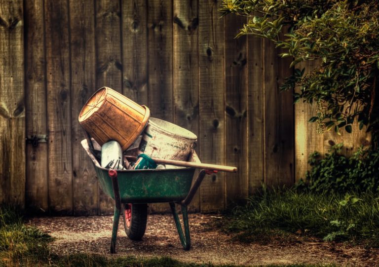 a green wheelbarrow full of gardening tools beside a fence. a spruce up of the garden