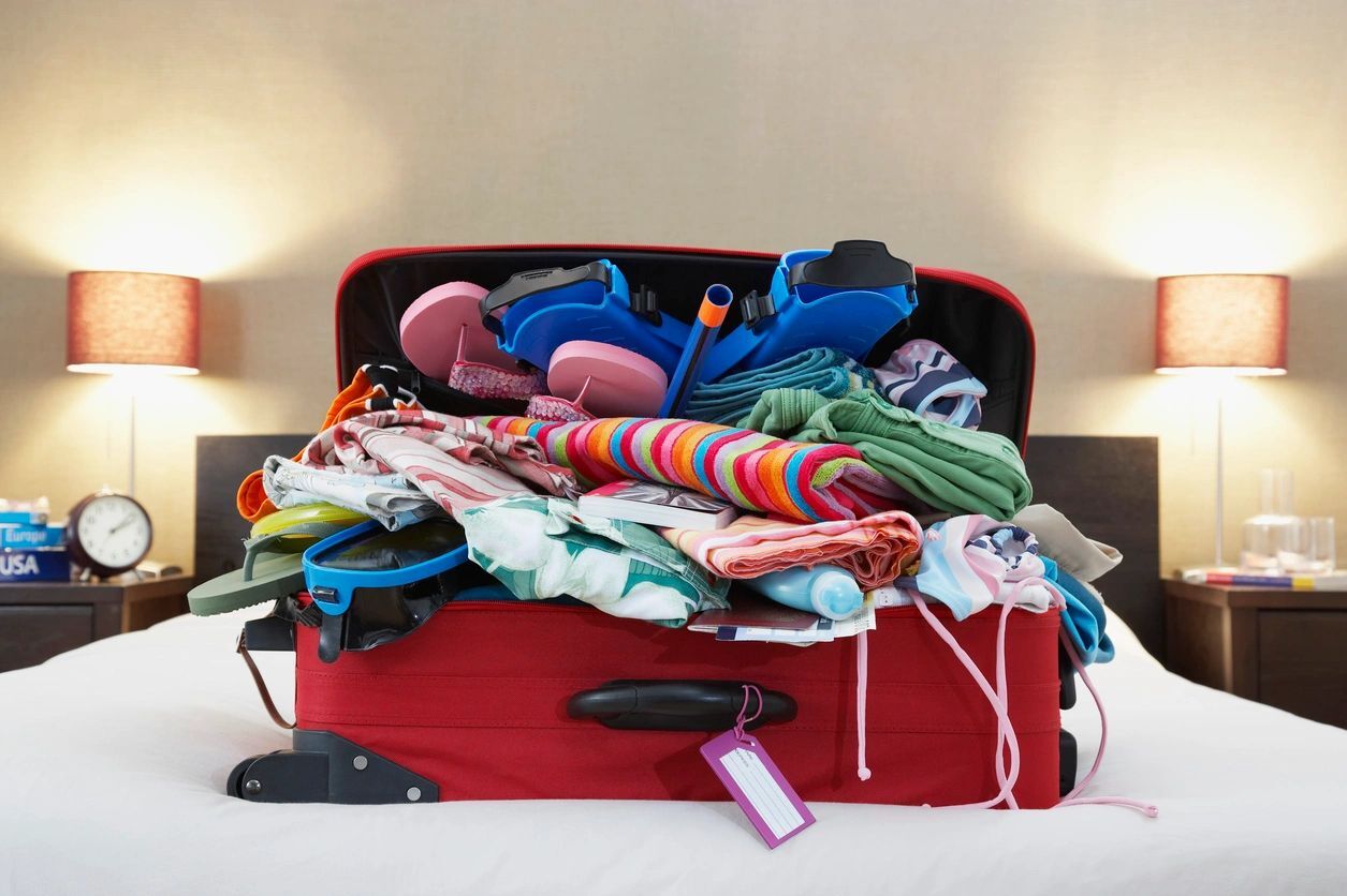 a suitcase overflowing with clothes sitting on a bed in a hotel. Bed bugs Vancouver - how do bed bugs travel