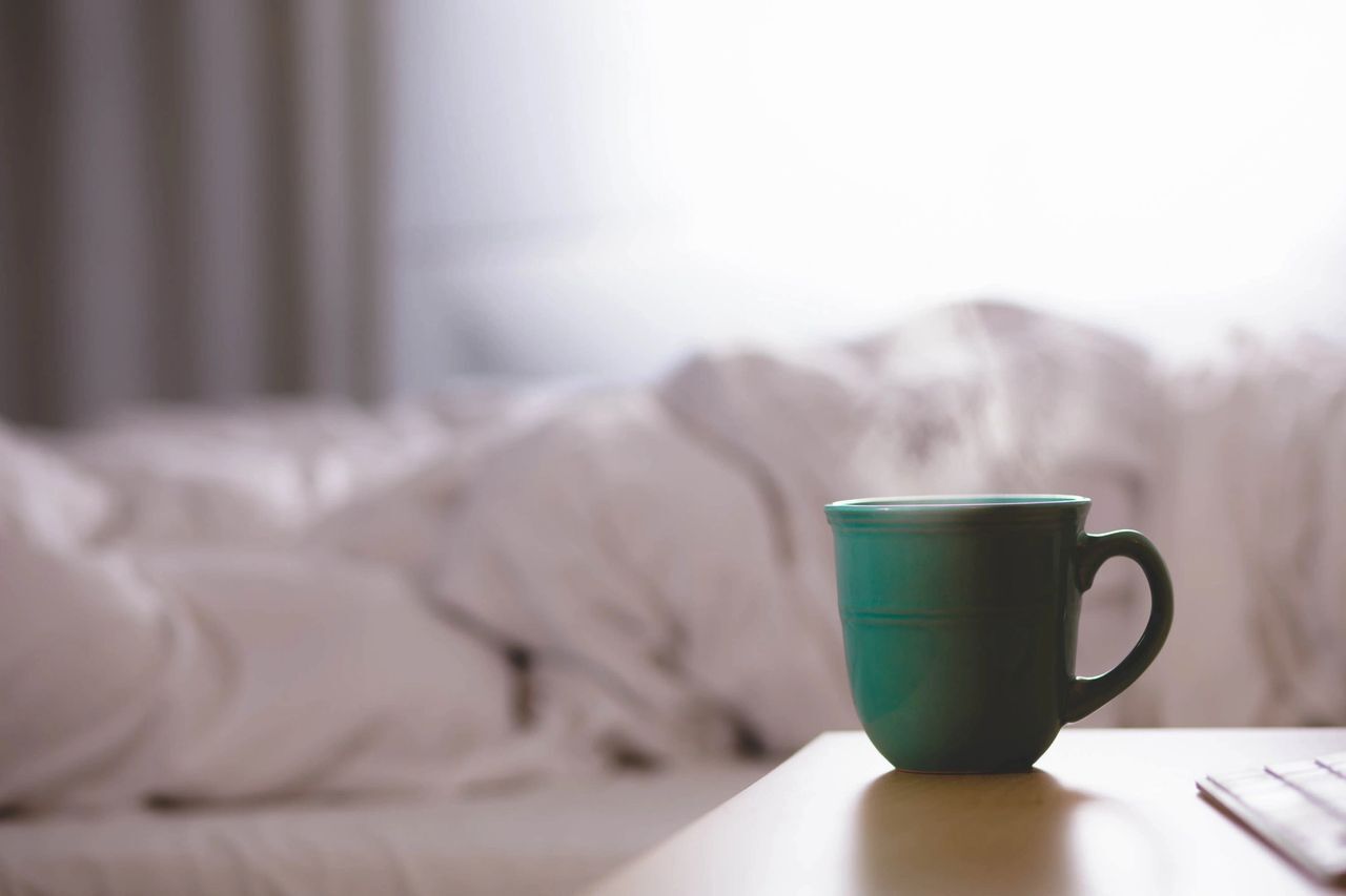 a green cup of coffee sitting on a nightstand with an unmade in the background. Bed bugs